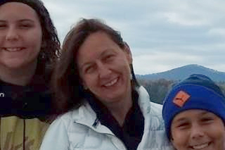 Image shows Michelle Sonnenberg smiling at the camera with her family in front of mountains
