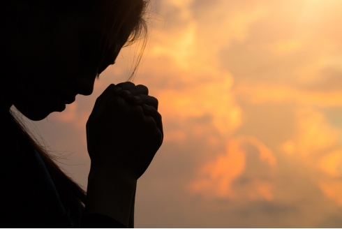 profile of person praying in front of cloudy sky