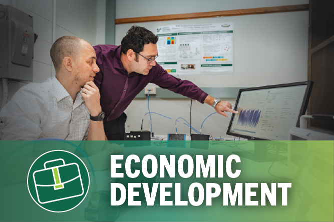 Two males pointing at a graph on a computer screen, words at bottom: economic development