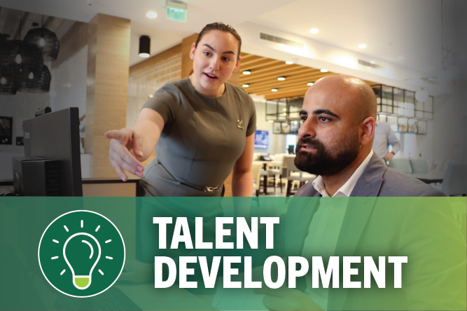 Female pointing at a computer screen with male sitting at computer with words at bottom: talent development