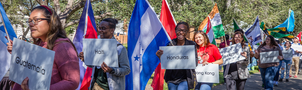 Students walking around campus holding up their country's flag and sign that says which country they're from.