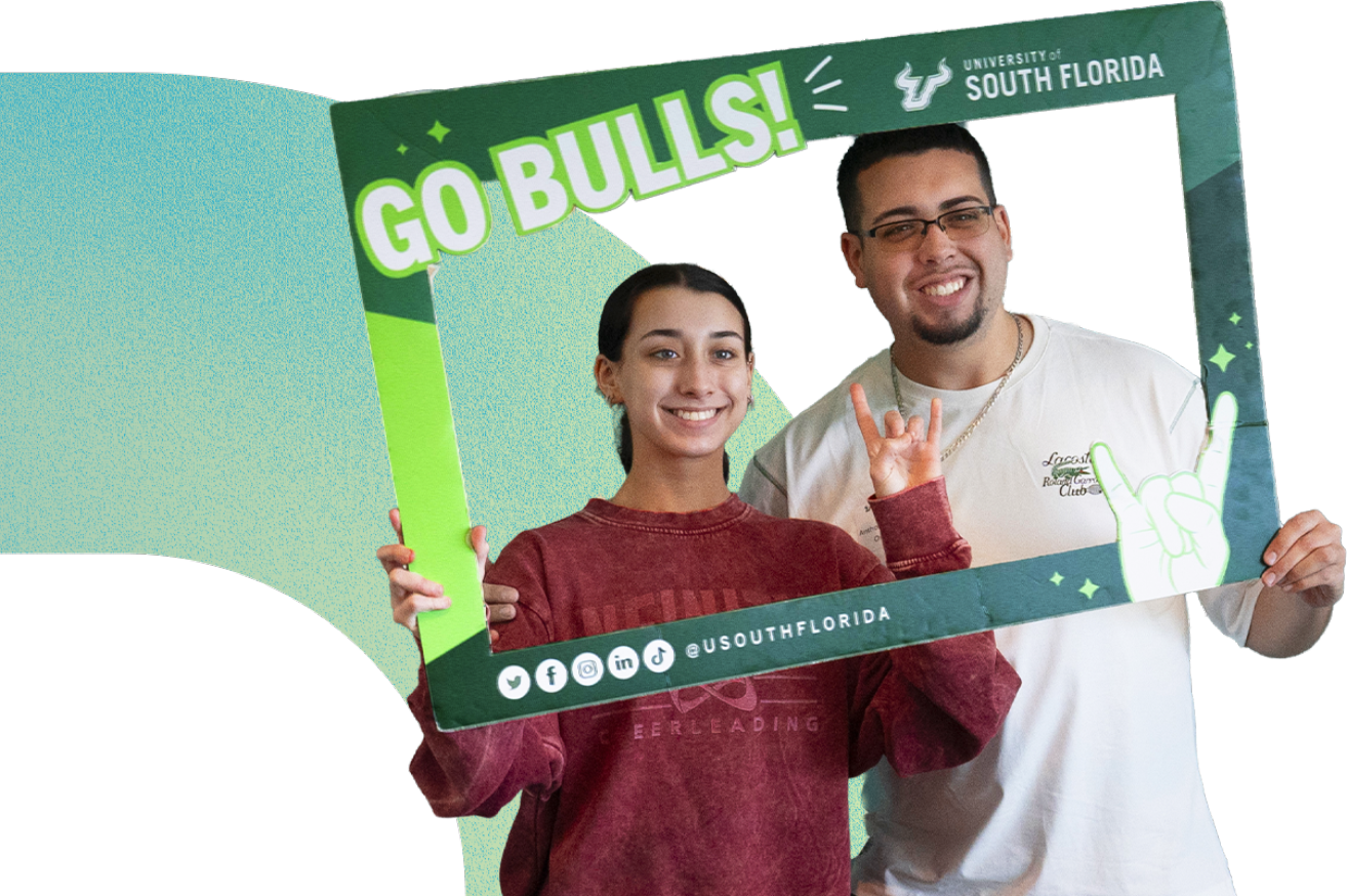 Two students smiling while holding a USF photo frame prop.