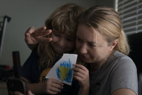 With son, Volodymyr, holding a Ukrainian flag he made, Hanna Tverdokhlib, a 37-year-old Ukrainian immigrant, flashes a three-finger salute to her sister on a video chat in her apartment in Long Beach, Calif March 1, 2022. (AP)