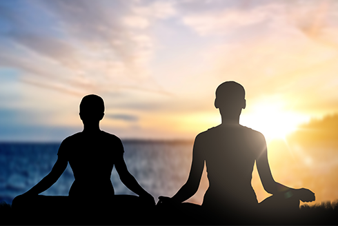 two people meditating on a beach at sunset