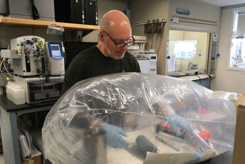 Dr. Jeffrey Ryan aboard the JOIDES Resolution extracting core samples for pore fluid analysis while working in a glove bag nitrogen atmosphere.