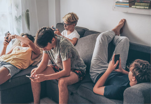 kids lounge on a sofa looking at their smartphones