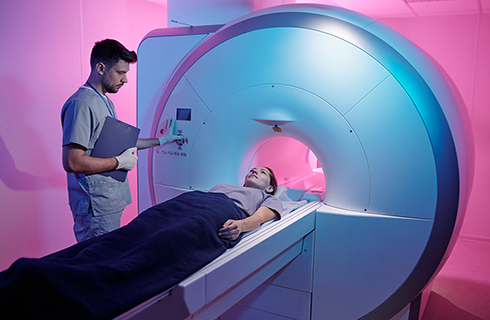 person lays on MRI bed while technician operates MRI machine