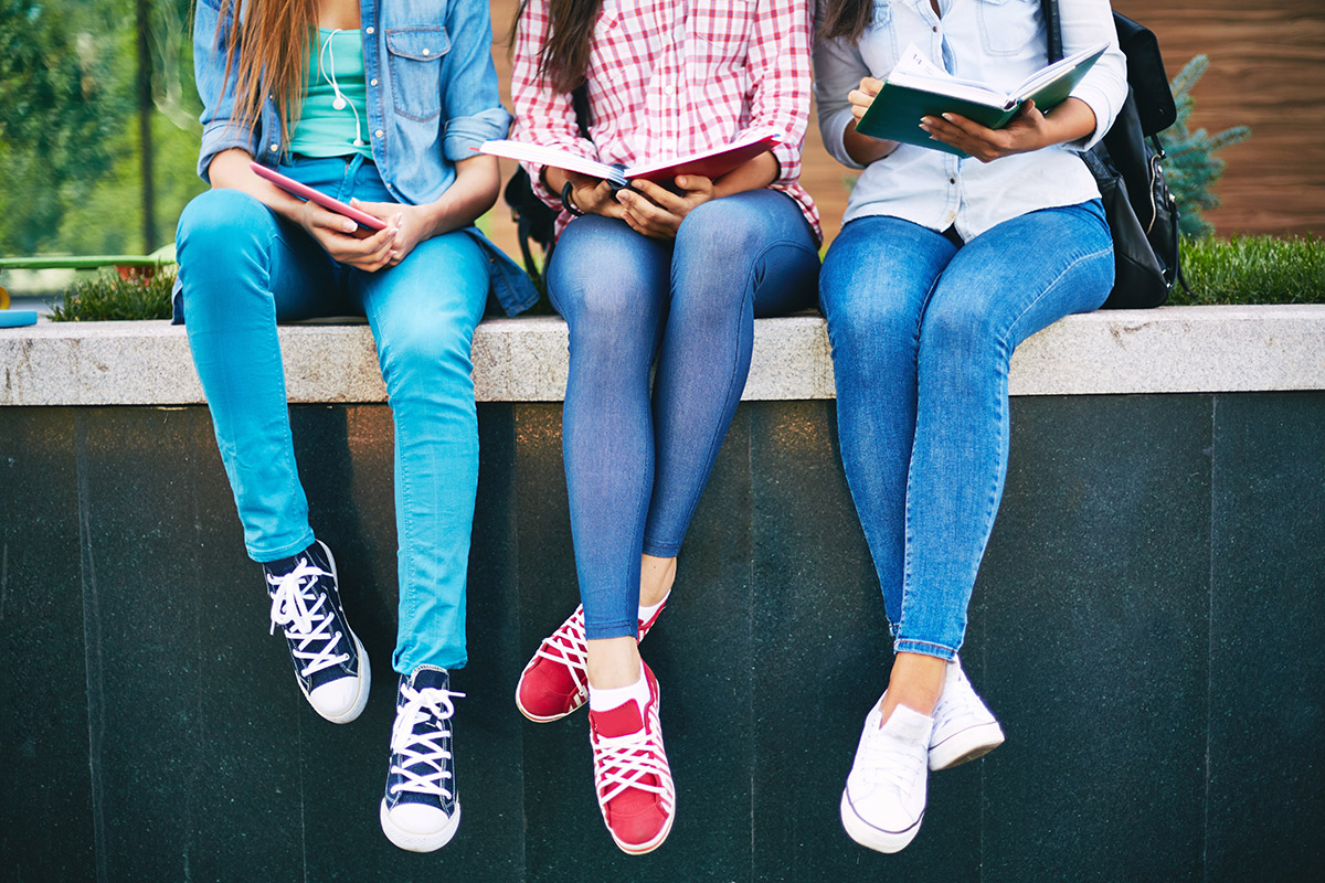 three girls in jeans seated on a wall