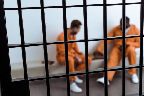 two inmates in orange jumpsuits sit behind jail bars