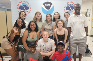 group of students and professor mbatu standing in front of a noaa backdrop