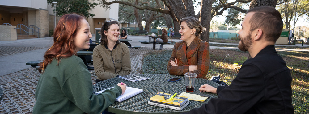 smiling students meet with faculty member at table outside Cooper Hall