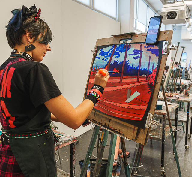 A student paints a vibrant red painting.