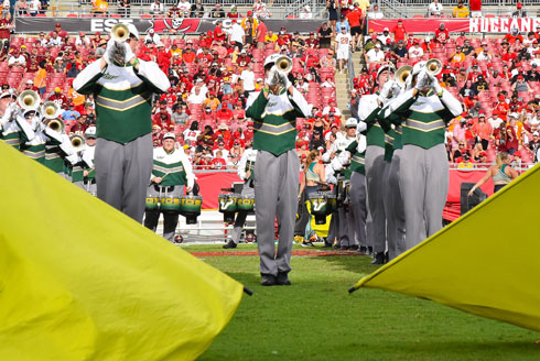 Three band members play trumpet among two large gold flags.