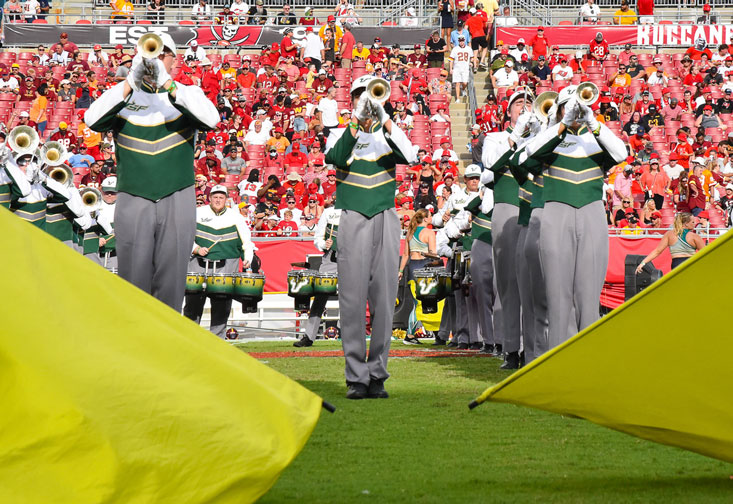 Three band members play trumpet among two large gold flags.