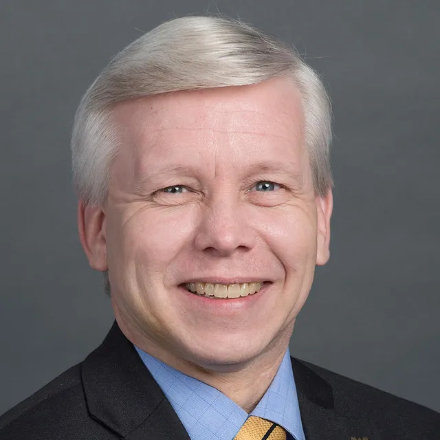 Scott Tobias wearing a black suit, blue shirt, and yellow tie.