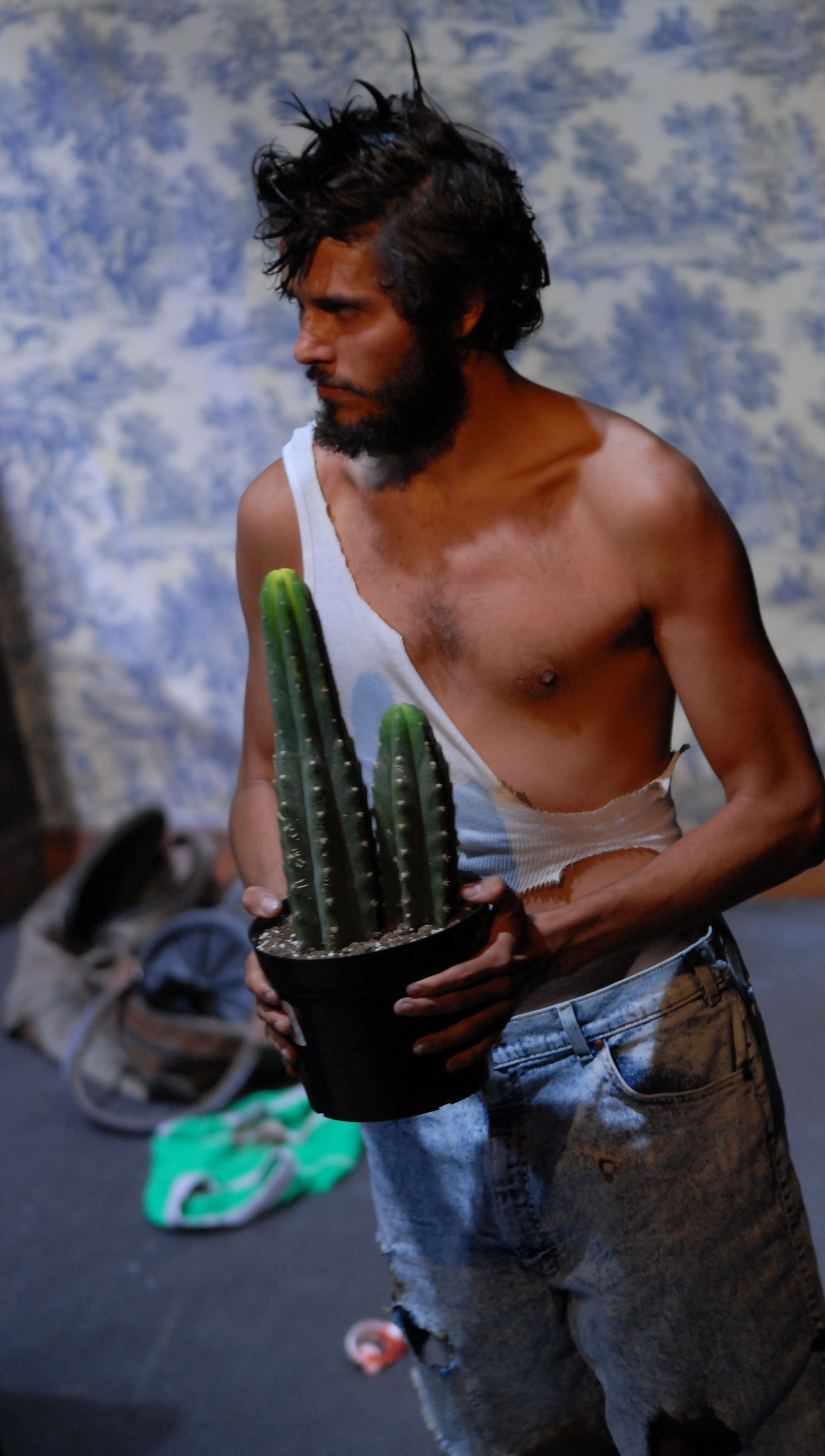 A man looks stage right while holding a cactus.