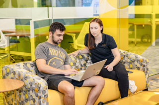 Two people sitting on a couch and working on a laptop