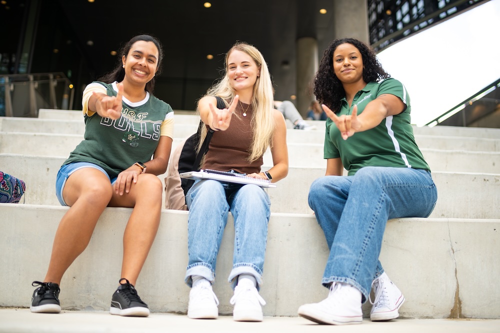 Three students make the “USF bulls” sign with their hands