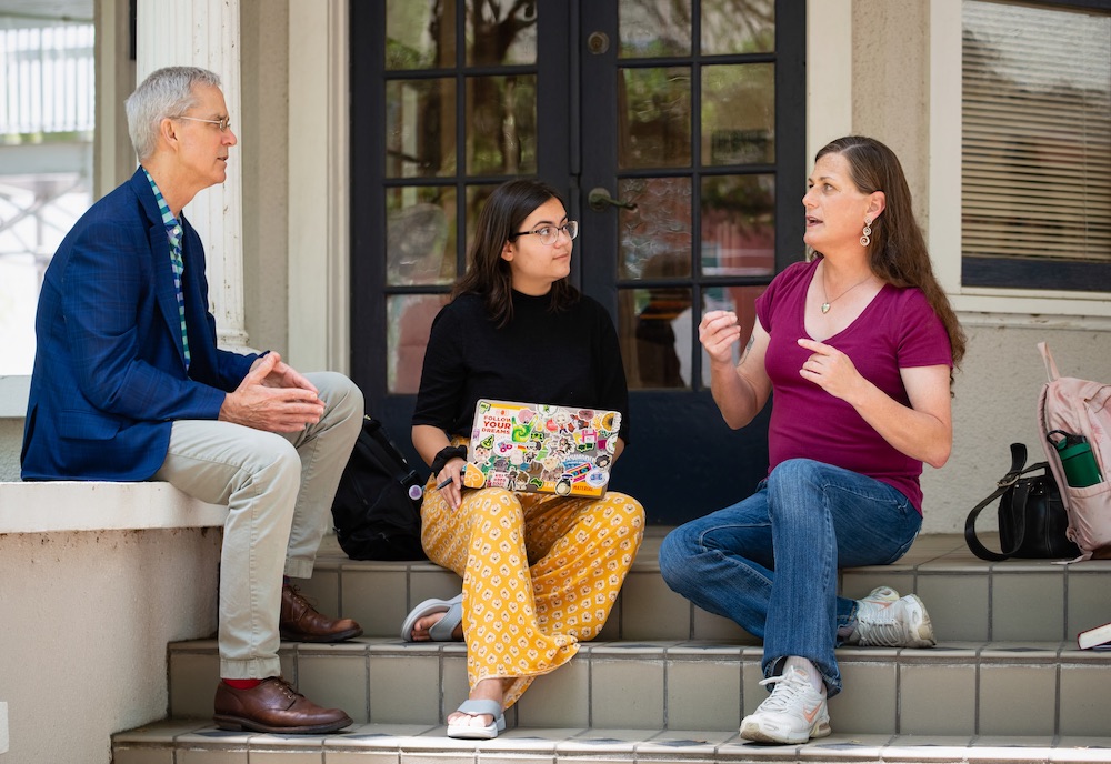 An instructor sits with two students 