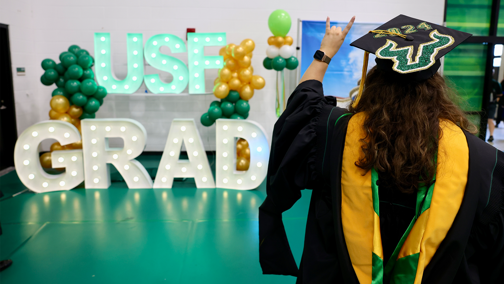 USF graduate wearing regalia facing a sign reading "USF Grad"