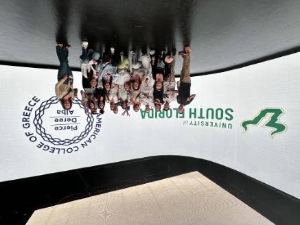A group of students from ACG standing in front of a large room wrapping screen with the USF and ACG logos