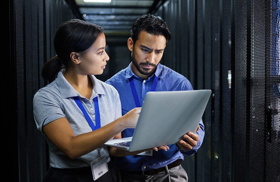 man and women stand in a server room looking at laptop
