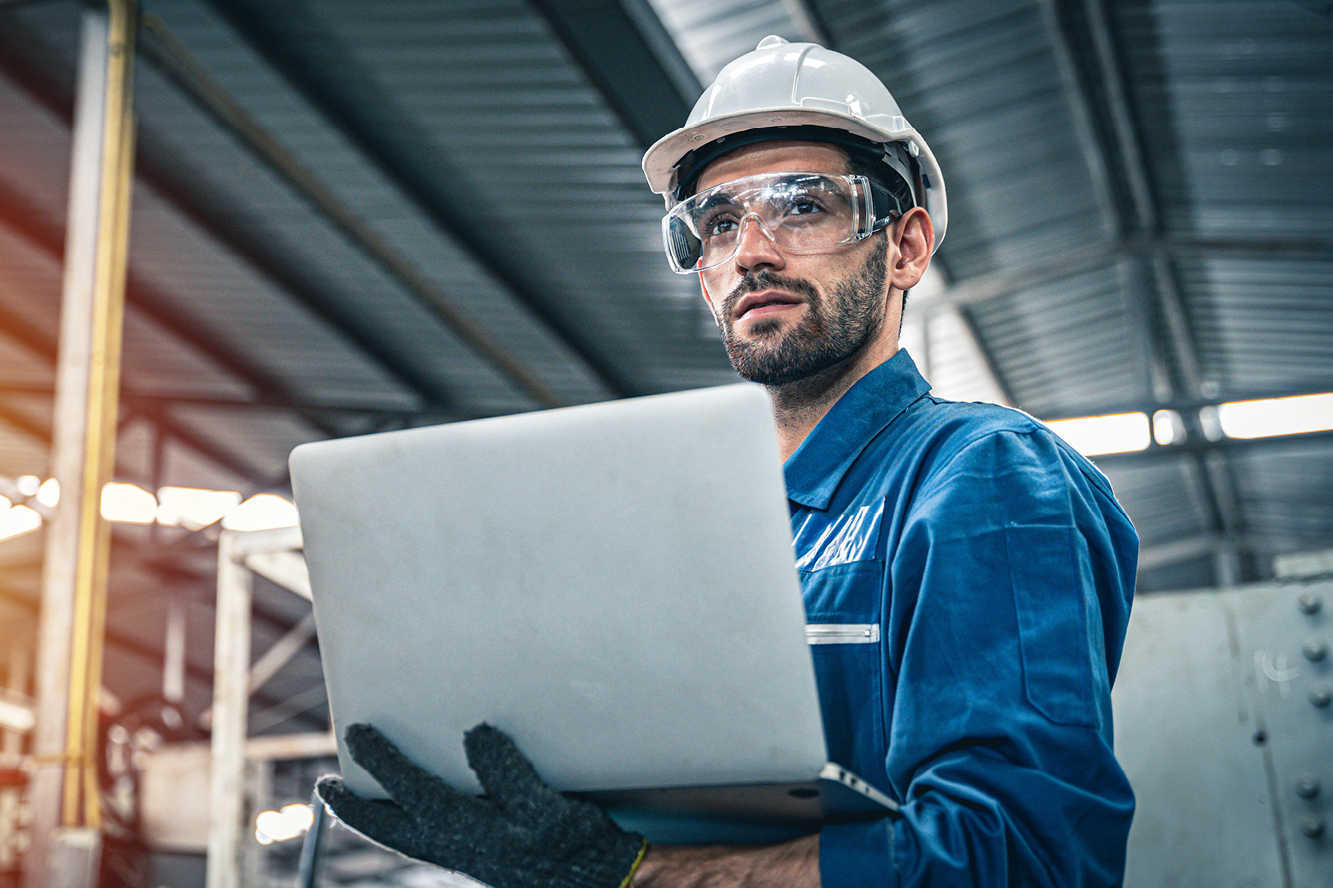 A man wearing a hard hat and goggles holding a laptop
