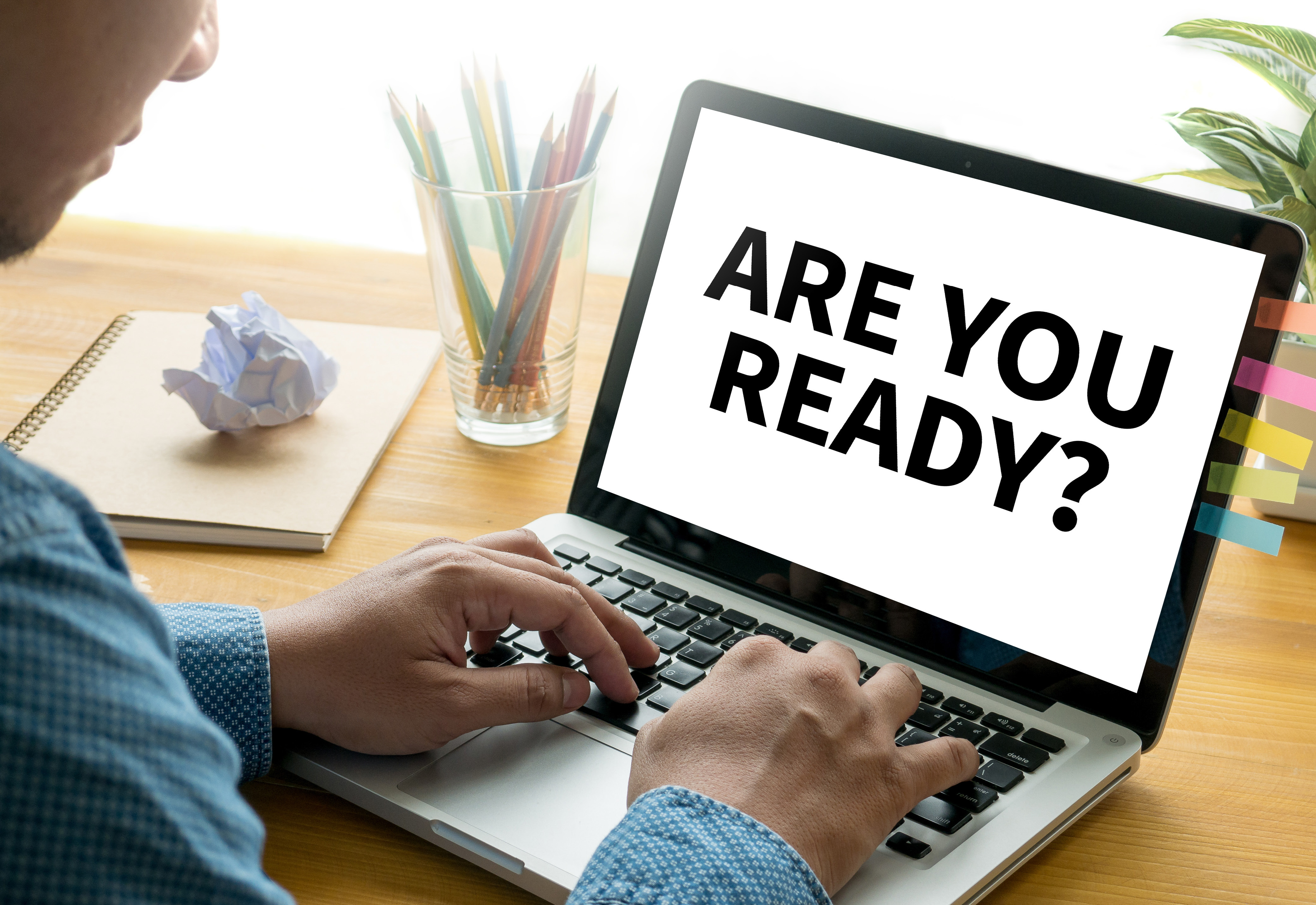 A person sitting in front of a laptop that says, "Are You Ready?" on the screen
