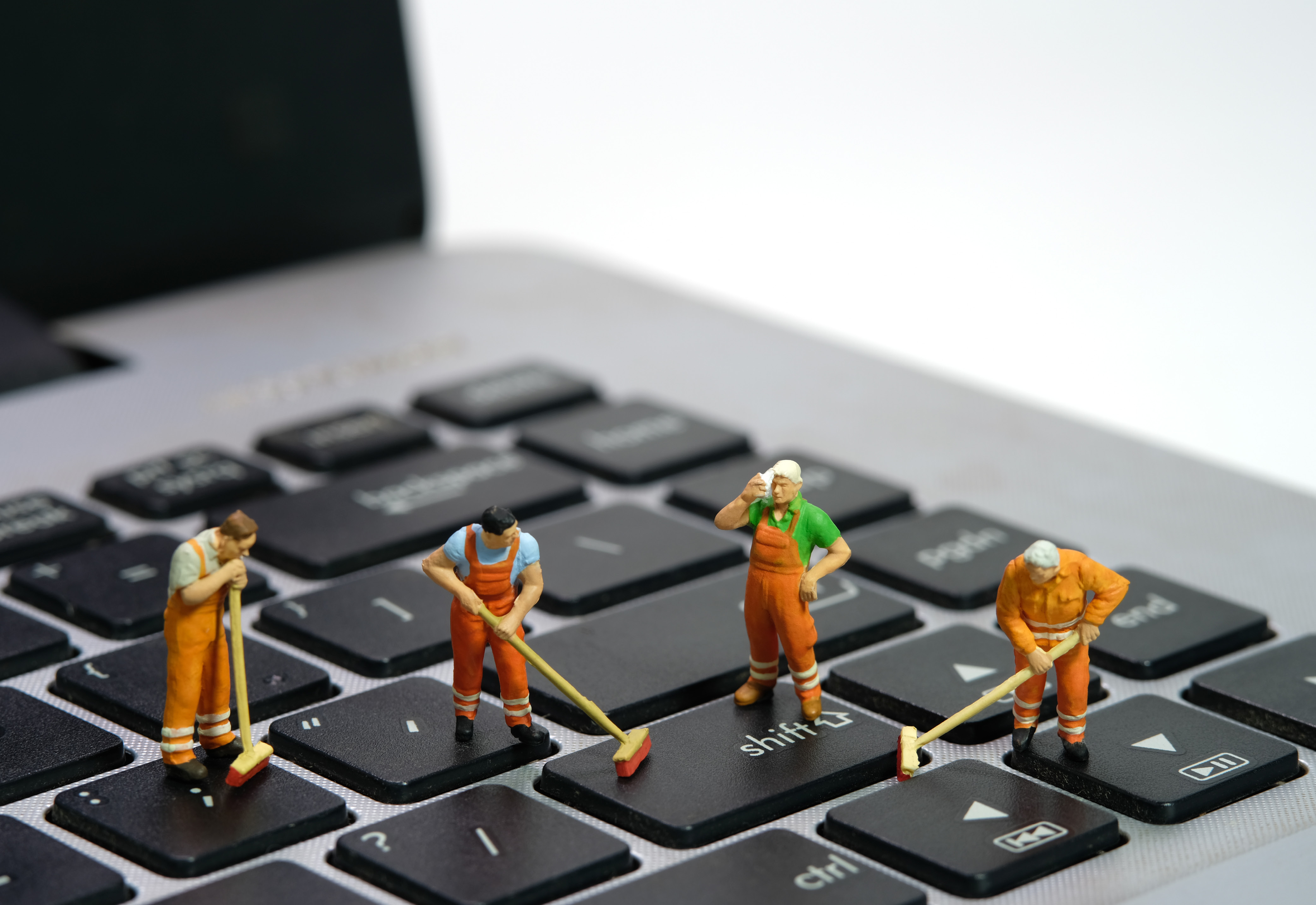 Figurines of people standing on a laptop keyboard and cleaning