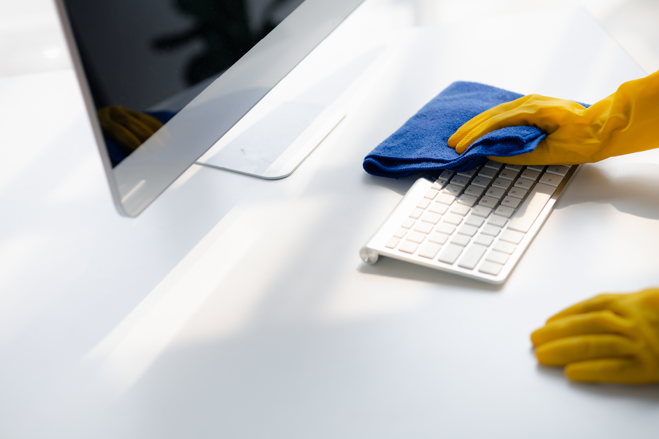 Someone wearing gloves wiping a computer keyboard with a cloth