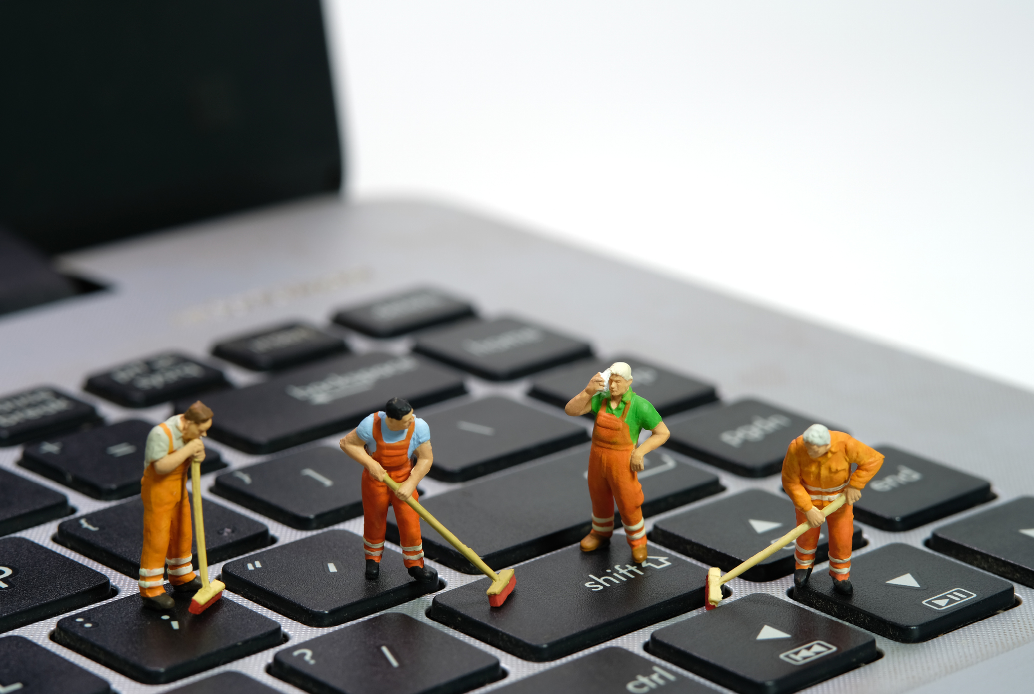 Figurines of people standing on a laptop keyboard and cleaning
