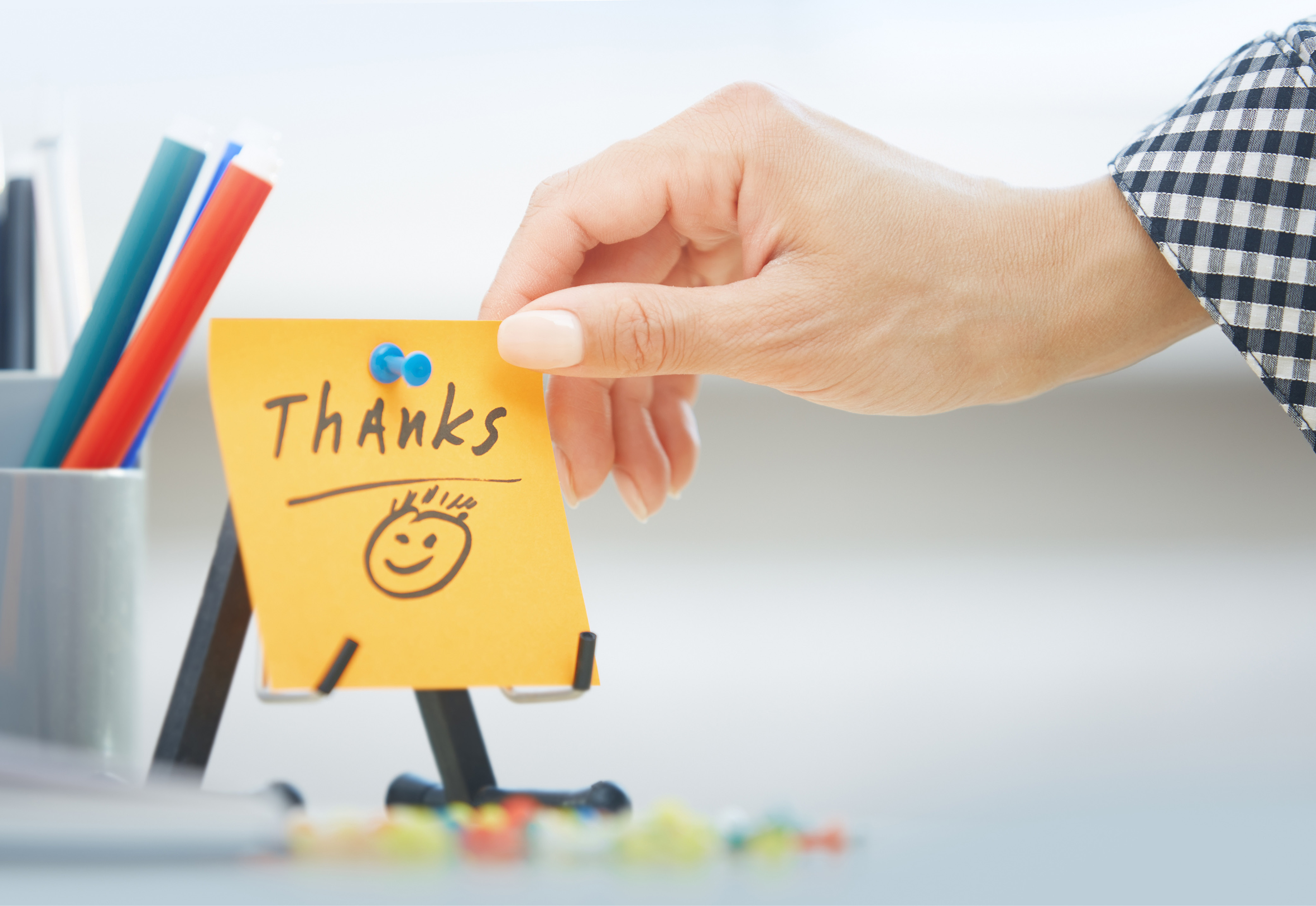 A person holding a sticky note that says "thanks" with a smiley face