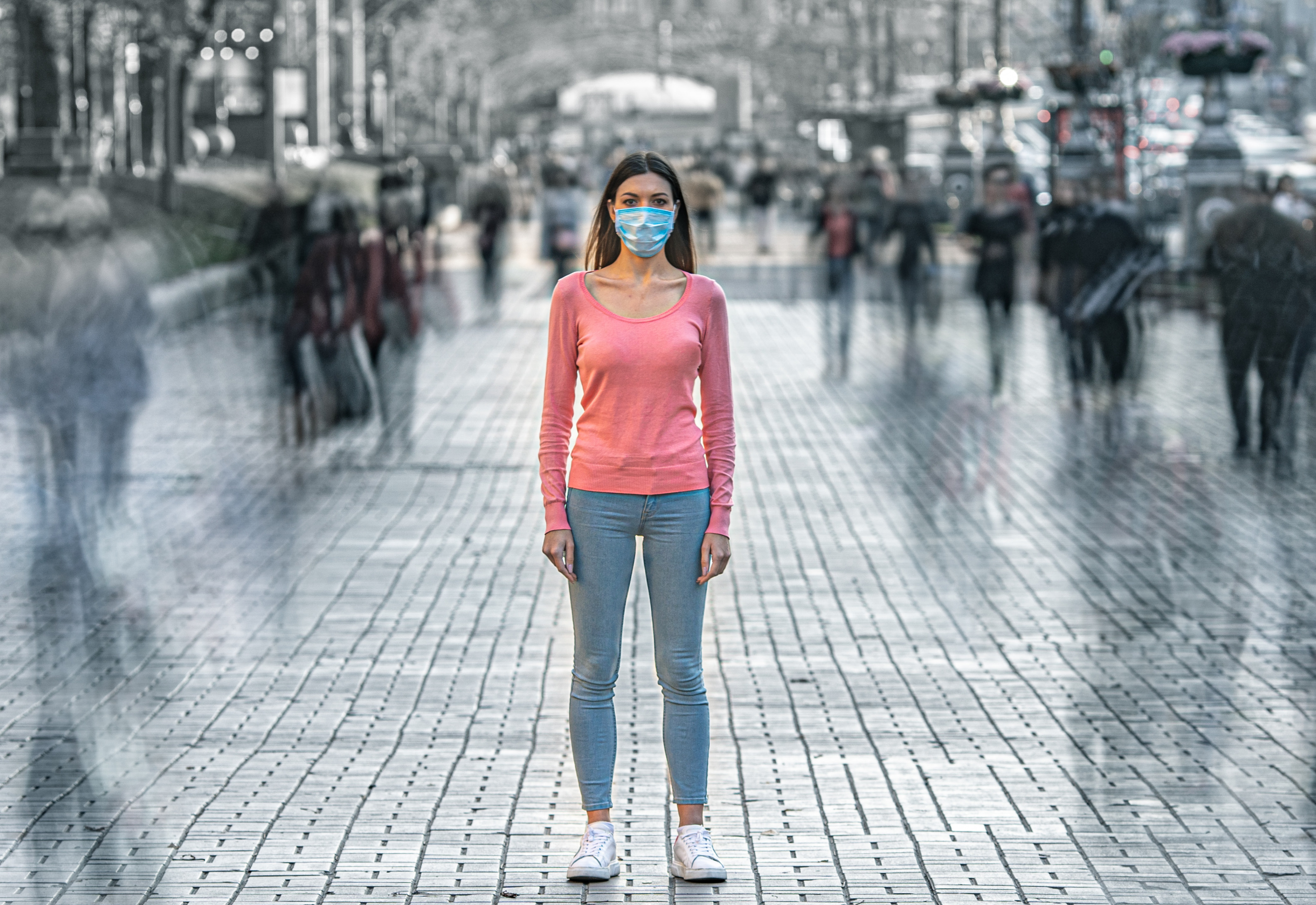 A woman standing on a city street wearing a face mask