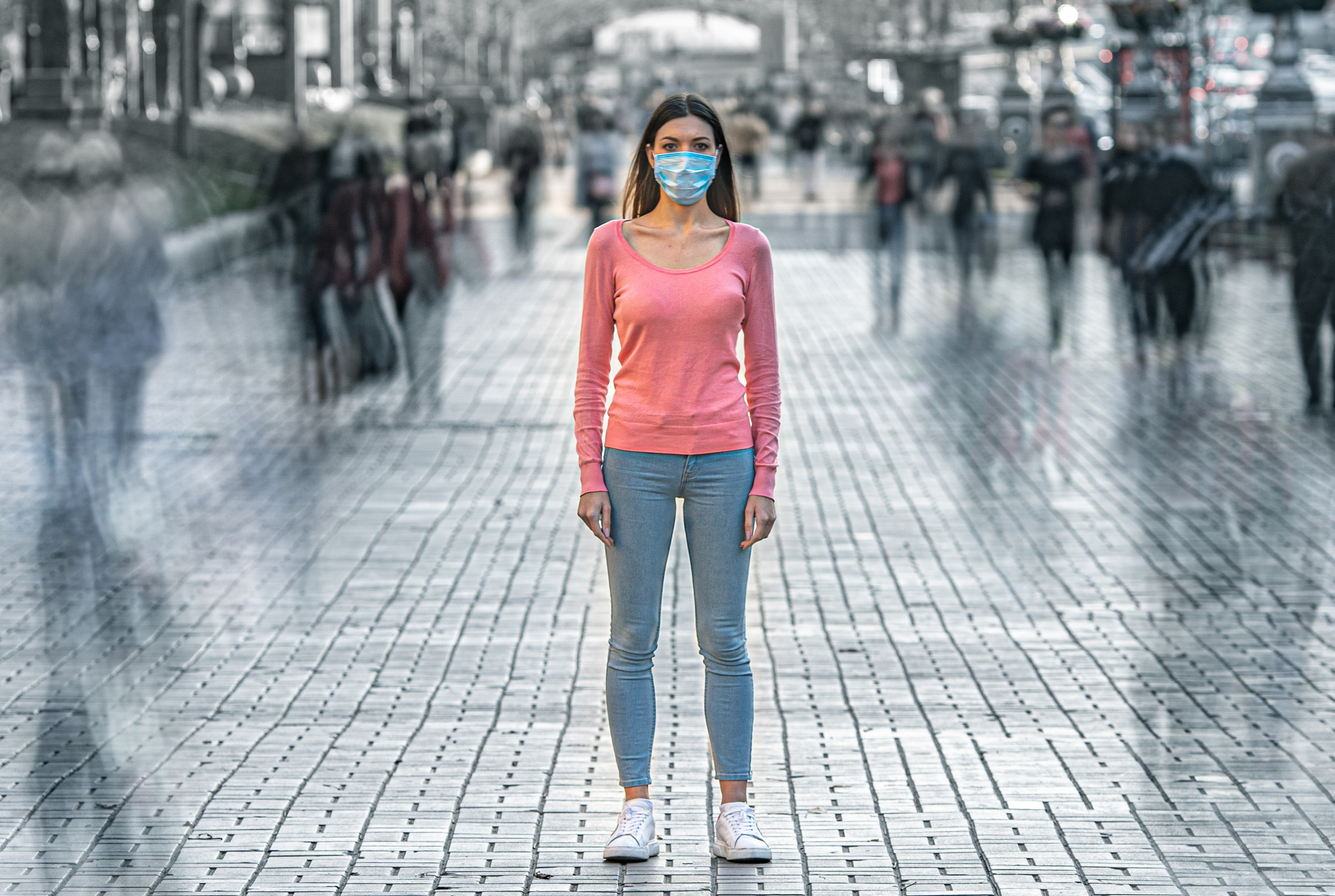 A woman standing on a city street wearing a face mask