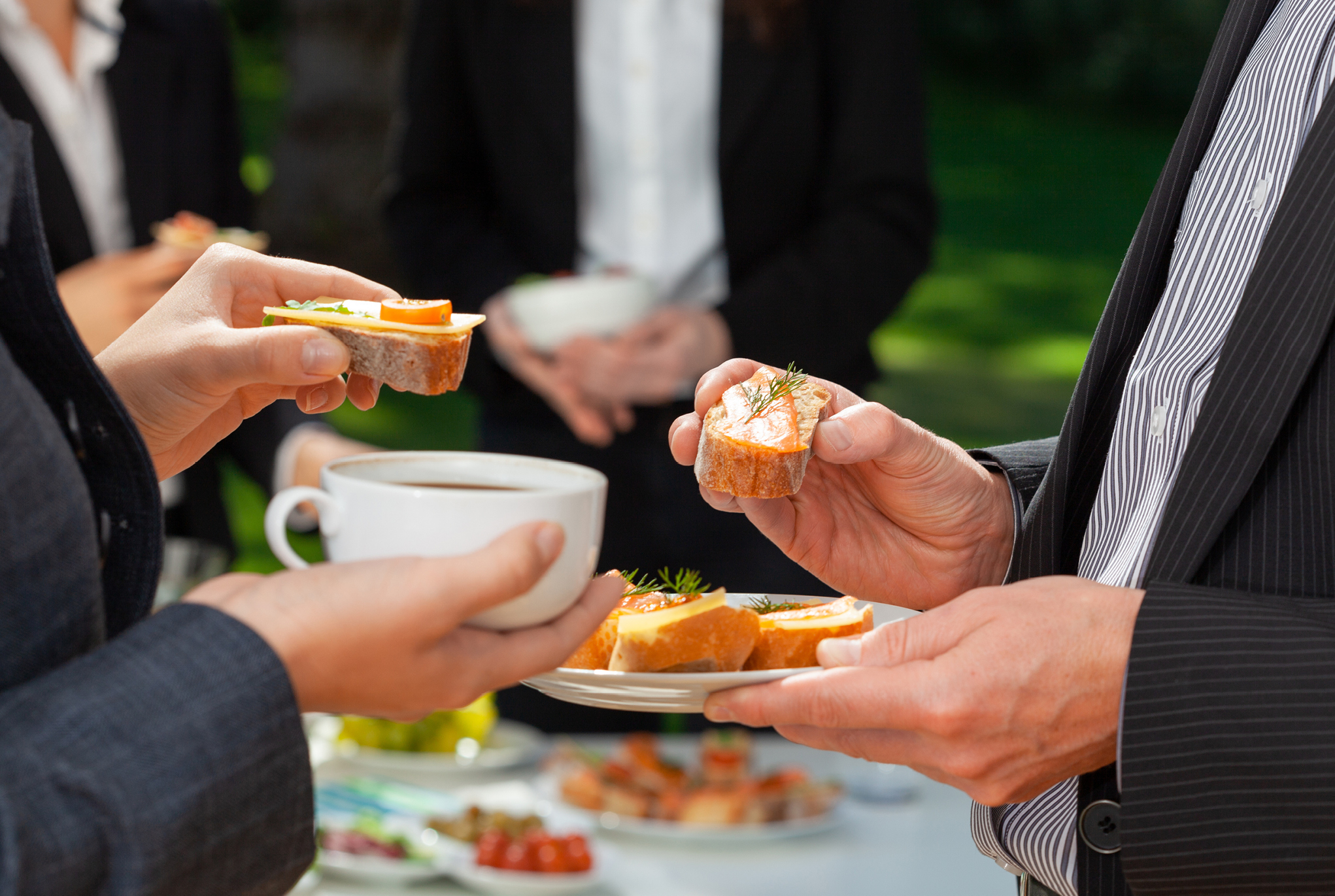 People in business attire holding plates of food and cups of coffee