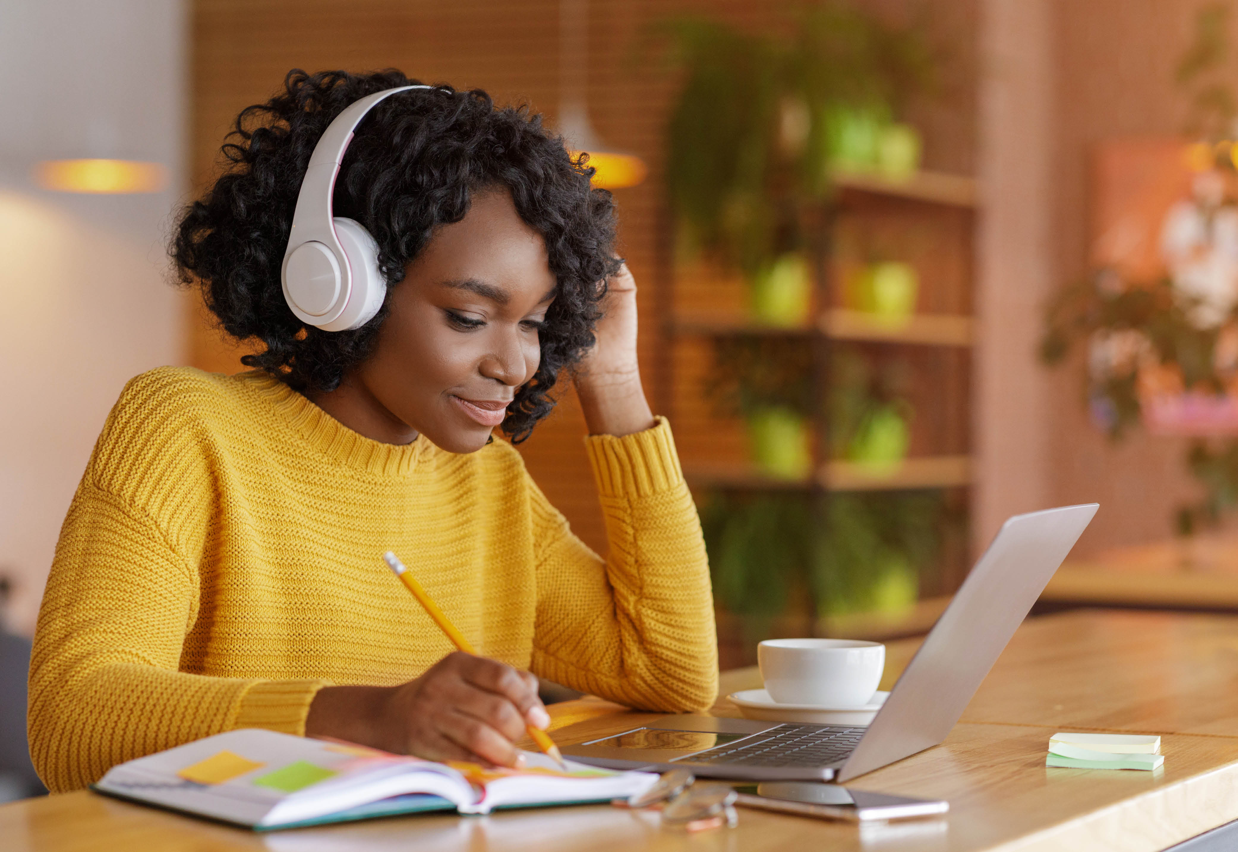 Woman wearing headphones sitting with her laptop and notebook open