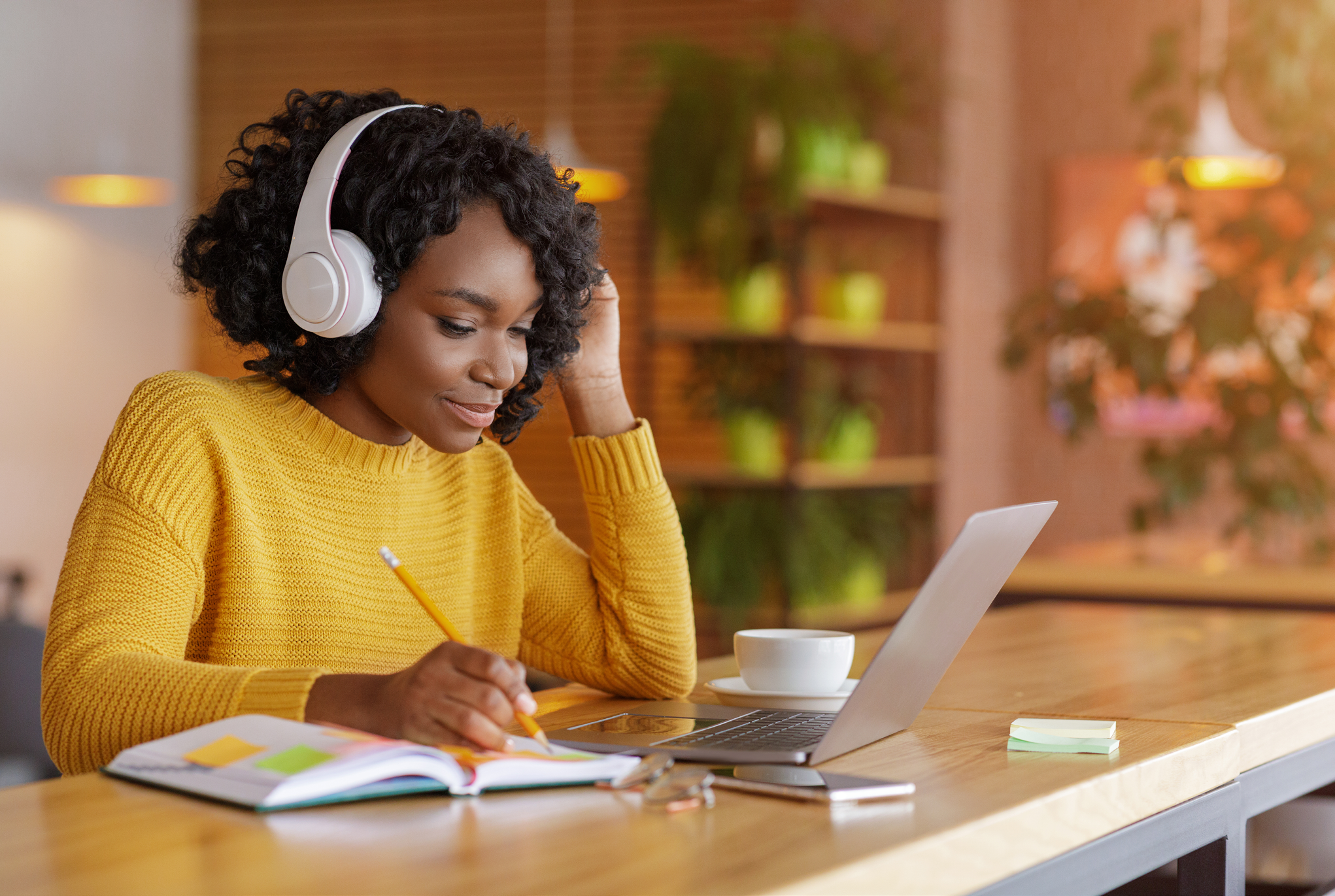 Woman wearing headphones sitting with her laptop and notebook open