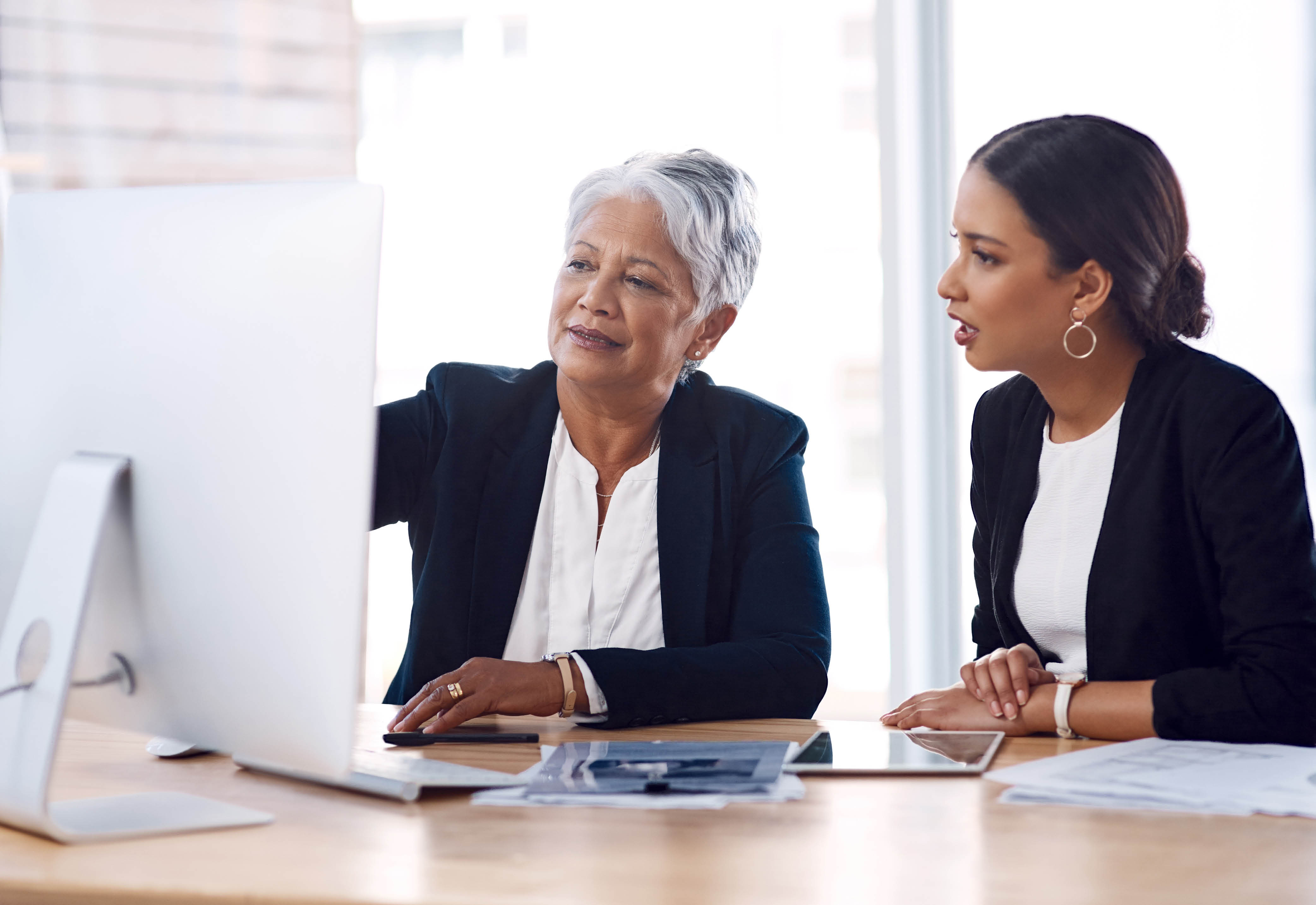 Two women dressed in business attire looking at a computer