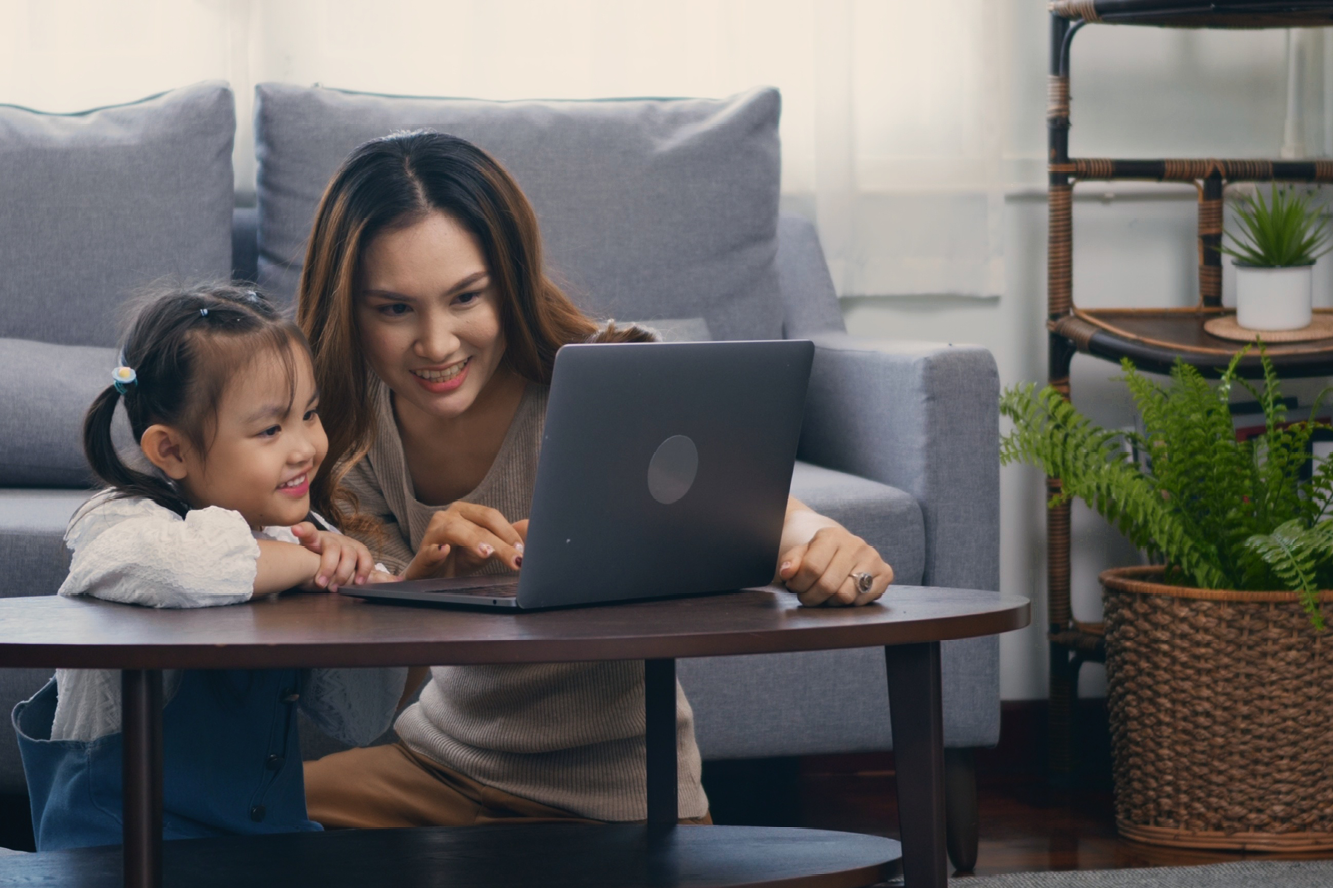 A mom and her young daughter sitting next to a laptop