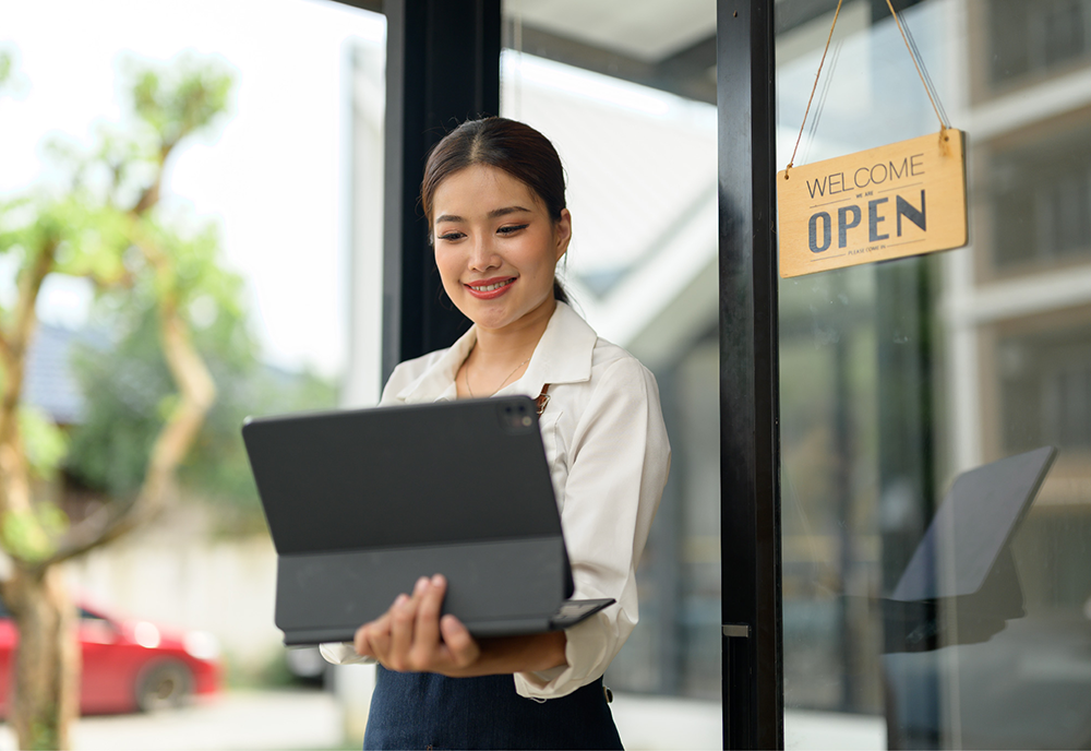 woman standing outside of open business holding a laptop