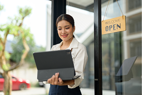 woman standing outside of open business holding a laptop