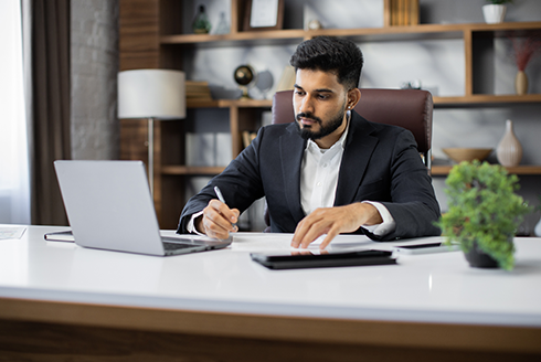 business man sits at computer writing something down