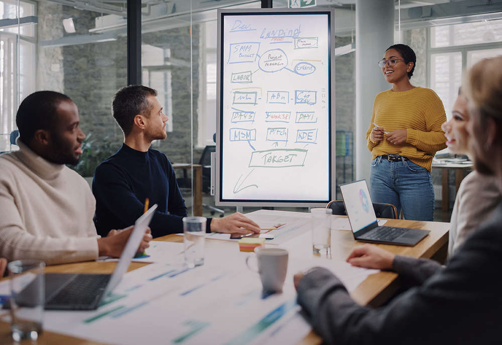 a group of people sit around a white board discussing a project