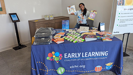 sonia poses with pamplets behind a table at a earling learning coalition event