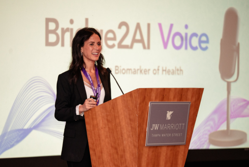 Dr. Yael Bensoussan at a podium with a Bridge2AI backdrop