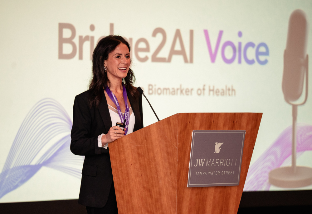 Dr. Yael Bensoussan at a podium with a Bridge2AI backdrop