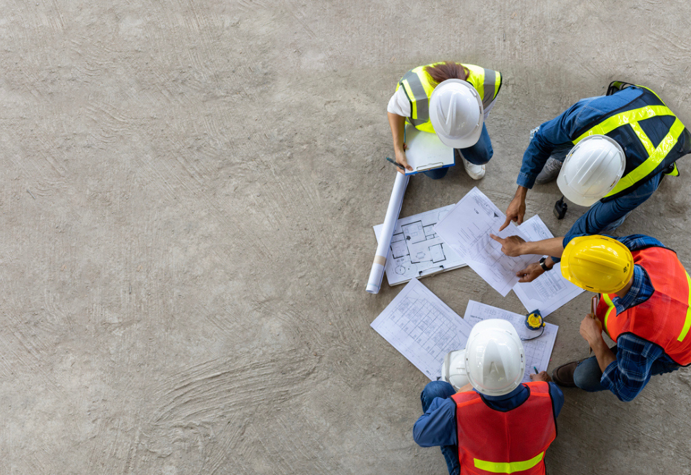 Top view of engineer, architect, contractor and foreman meeting at the construction building site with floor plan.