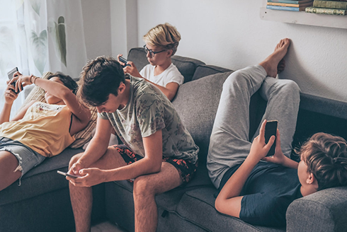 Four young boys on their phones while sitting on a gray sofa