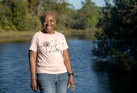 A woman stand near a pond smiling on a sunny morning. 