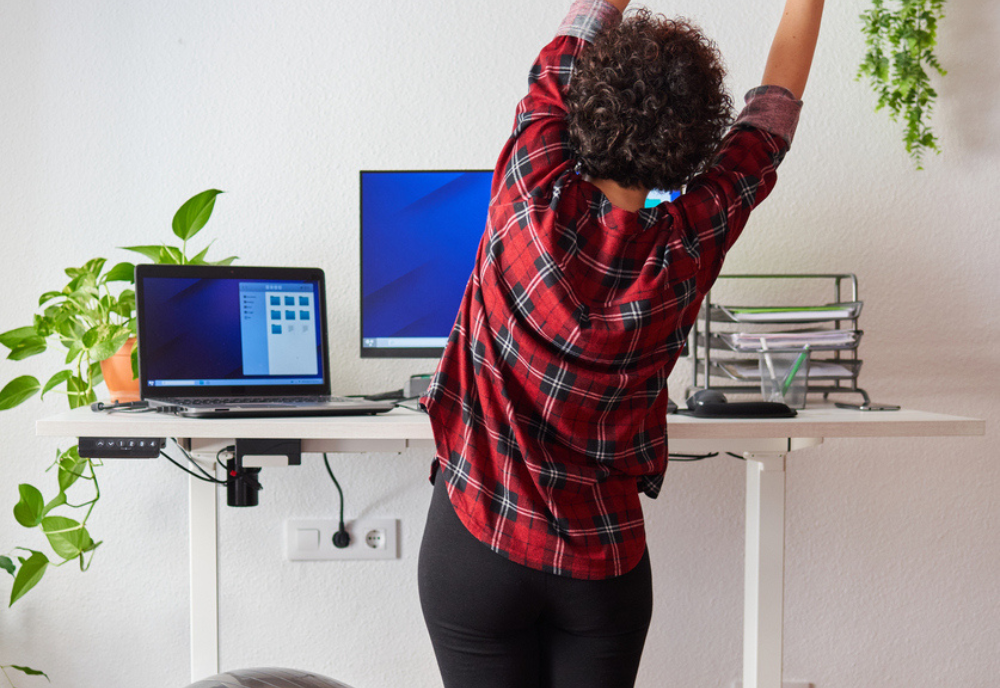 Woman telecommuting at an adjustable desk standing next to a fitball.